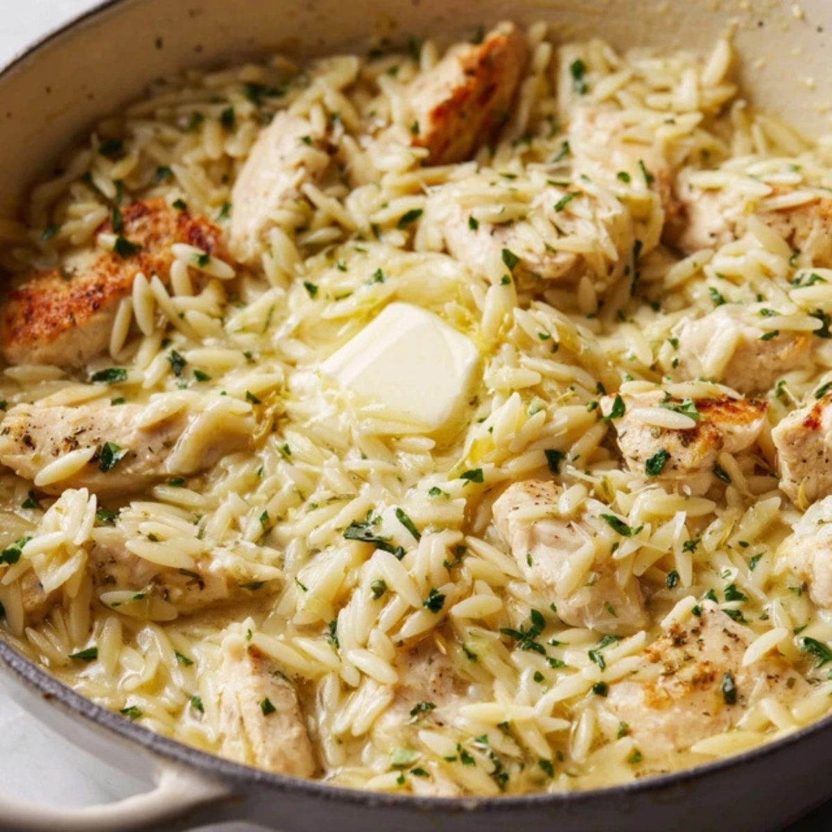 Creamy lemon chicken orzo in skillet with butter and zest