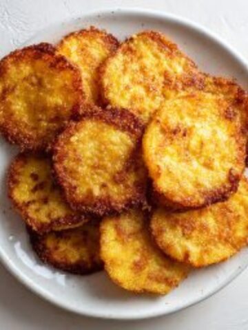 Crispy fried yellow squash slices stacked on a white plate on a white kitchen counter