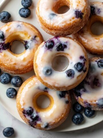 Freshly glazed homemade blueberry baked donuts on white kitchen counter