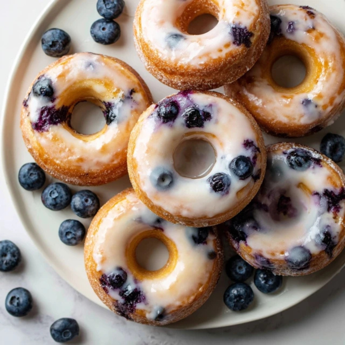 Freshly glazed homemade blueberry baked donuts on white kitchen counter