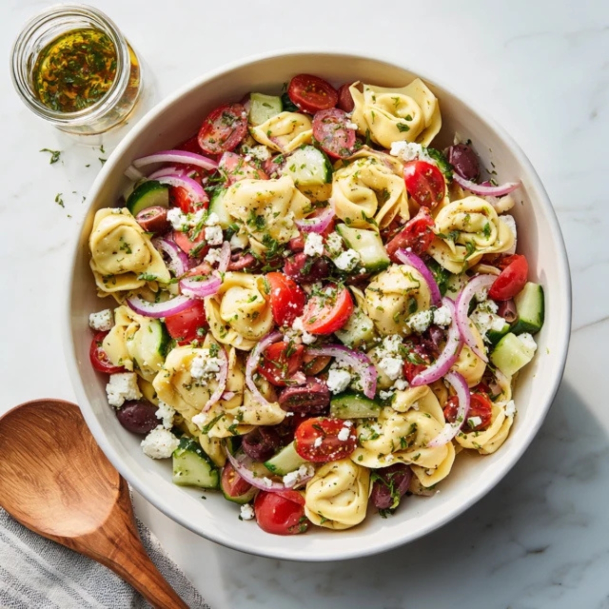 vibrant tortellini pasta salad with pesto, tomatoes, and mozzarella in a white bowl