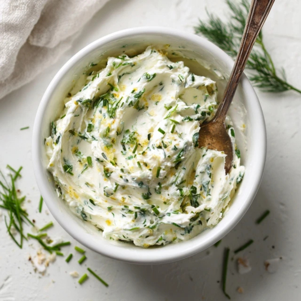 Cream cheese mixed with herbs in a white bowl on kitchen counter

