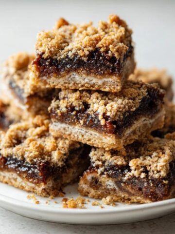 Homemade fig bars stacked on plate with oat crumbs