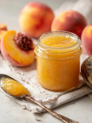 Jar of golden homemade peach butter on white kitchen counter