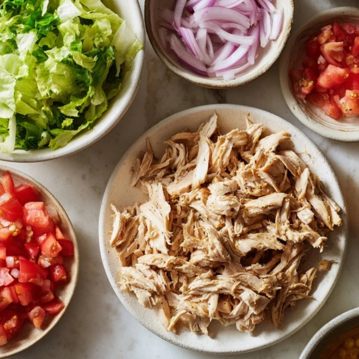 shredded chicken with chopped lettuce and diced tomato on counter