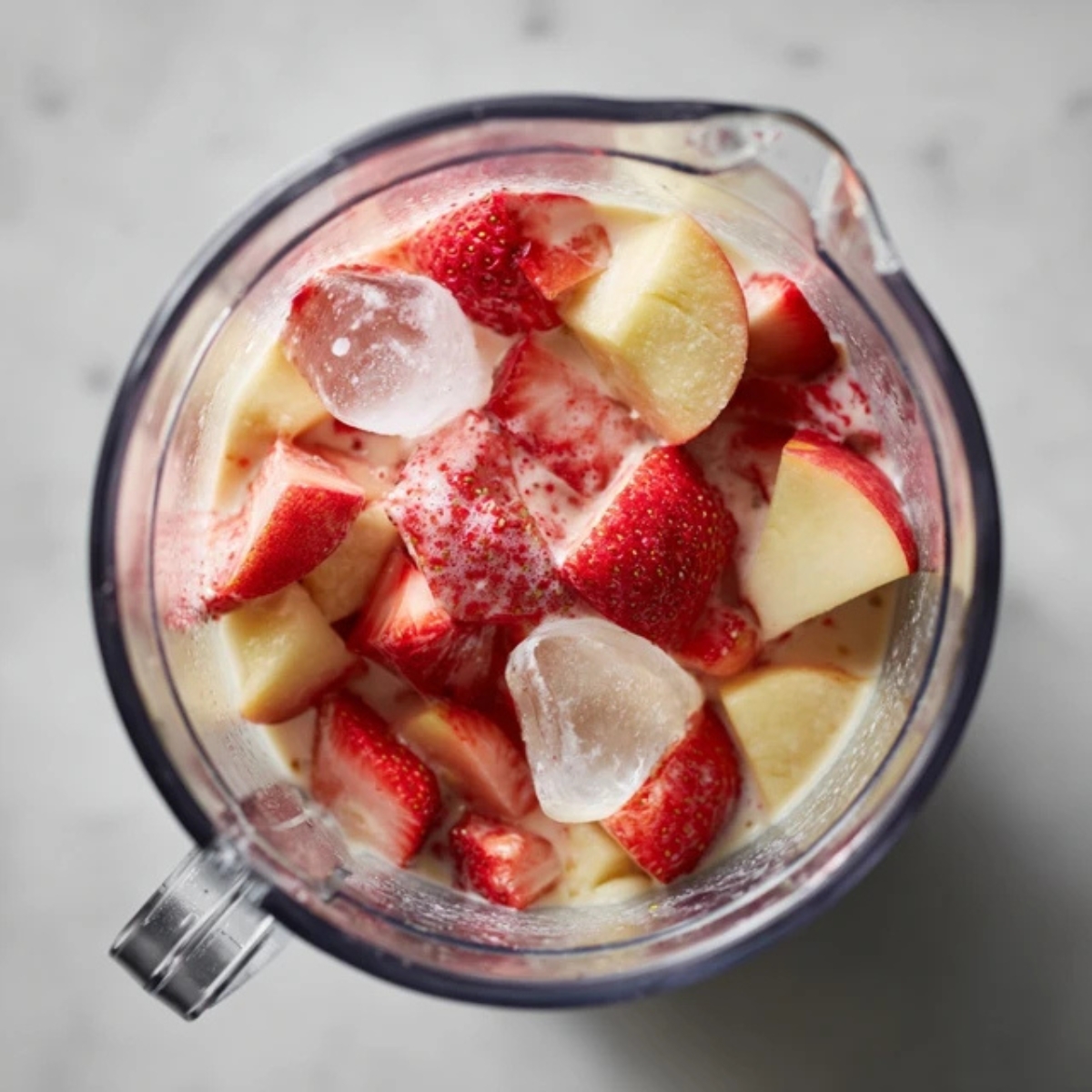 blender filled with strawberries, peaches, and ice ready to blend
