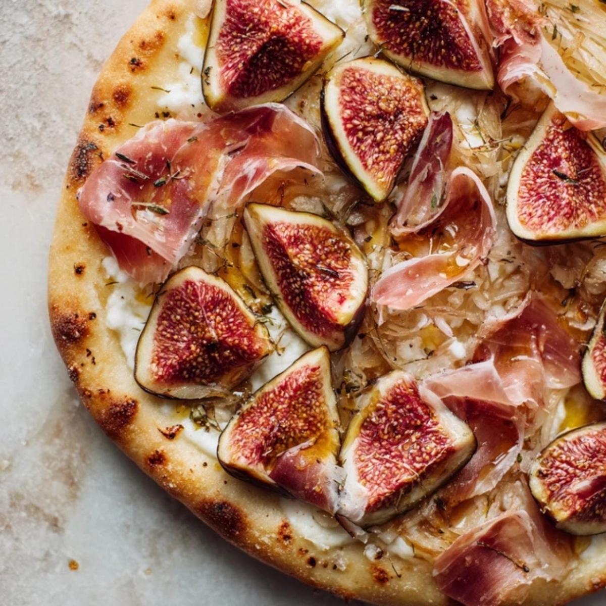 Pizza topped with fresh fig slices, torn prosciutto, and honey drizzle.