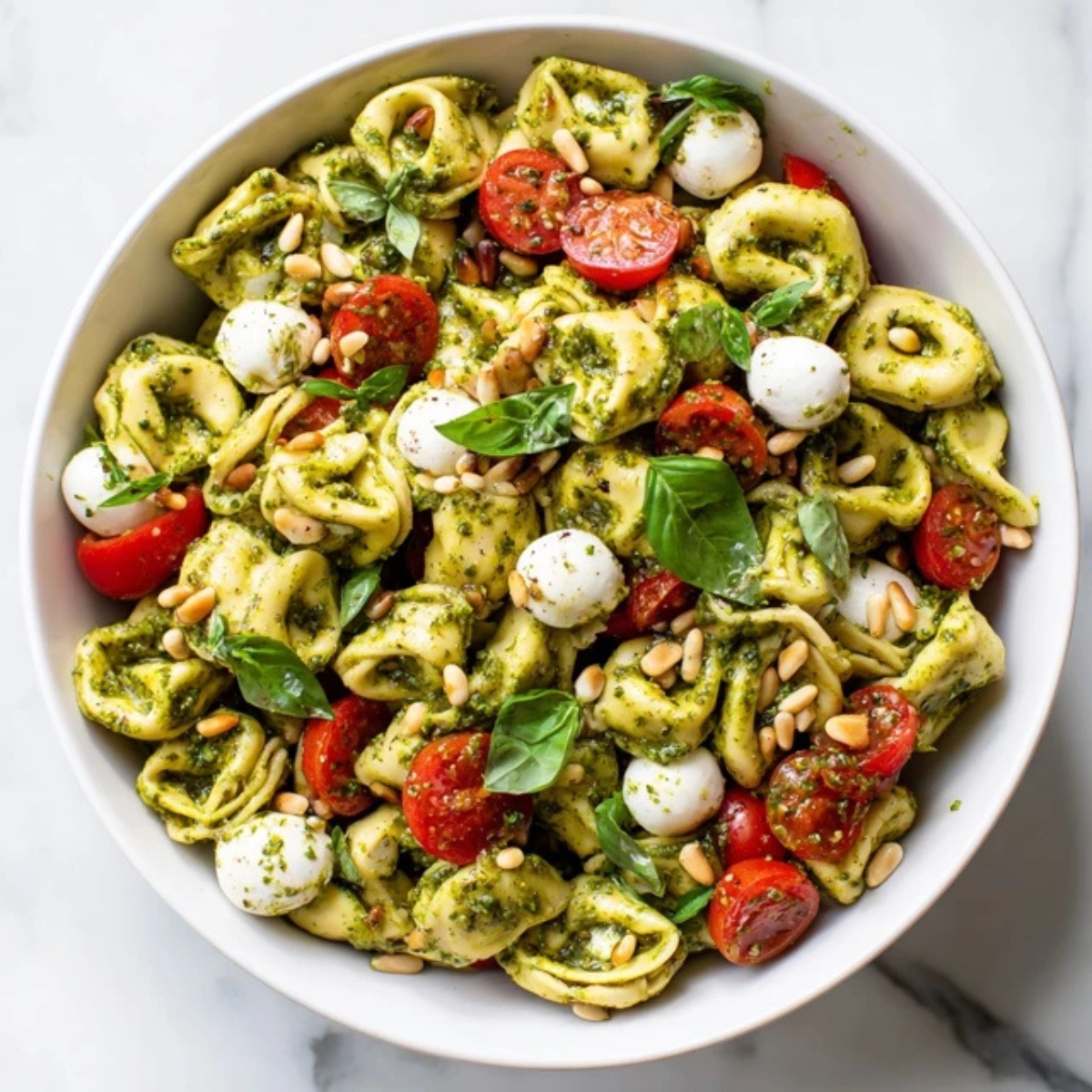 vibrant tortellini pasta salad with pesto, tomatoes, and mozzarella in a white bowl