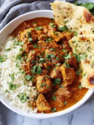 creamy chicken butter sauce with rice and naan on white kitchen counter