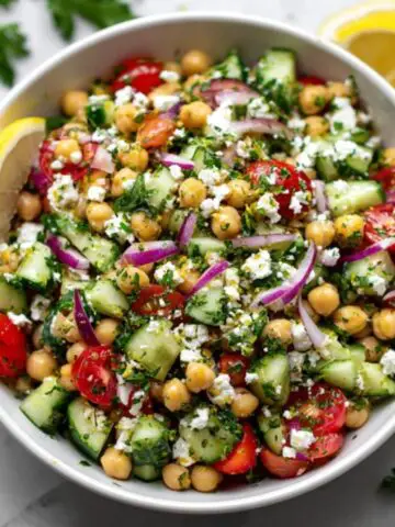 Mediterranean chickpea feta salad in white bowl with cucumbers, tomatoes, and parsley