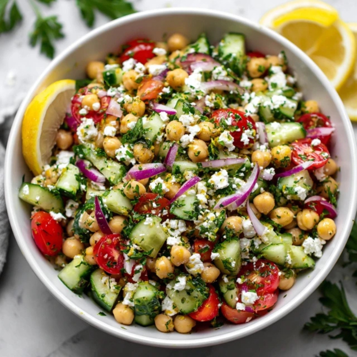 Mediterranean chickpea feta salad in white bowl with cucumbers, tomatoes, and parsley