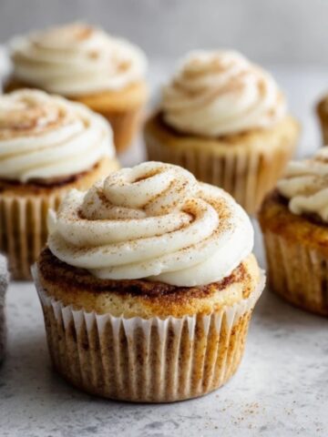 fluffy cinnamon roll cupcakes with cream cheese frosting on white counter