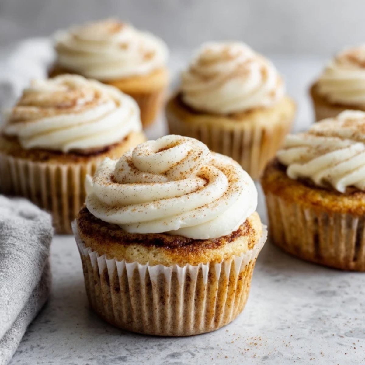 fluffy cinnamon roll cupcakes with cream cheese frosting on white counter