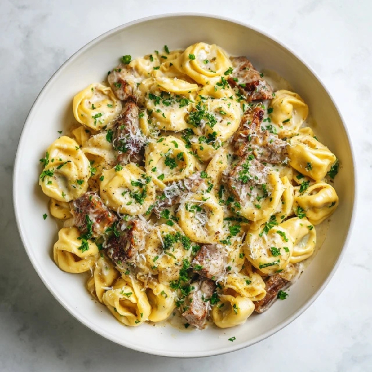 creamy steak tortellini with garlic parmesan sauce in white bowl