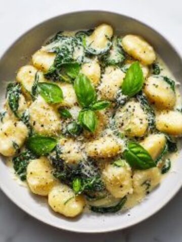Creamy gnocchi with spinach in Parmesan sauce on white counter