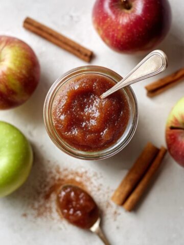 creamy instant pot apple butter in jar with apples and cinnamon