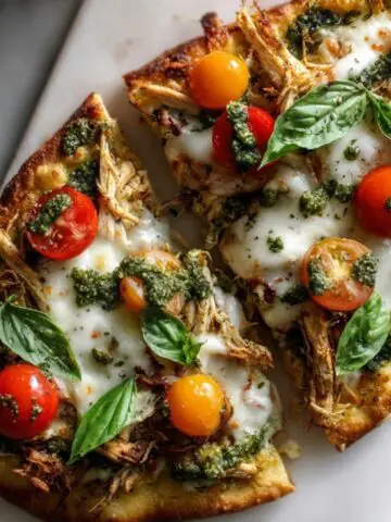 Homemade pesto chicken flatbread with mozzarella, tomatoes, and basil on white counter