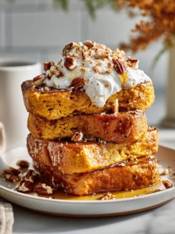 Pumpkin french toast with maple syrup and whipped cream on white counter