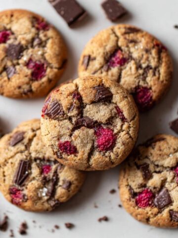 Homemade raspberry chocolate chunk cookies with fresh raspberries and dark chocolate chunks on white counter