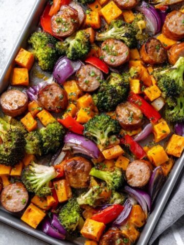 Sheet pan sausage and sweet potatoes with roasted veggies on white kitchen counter