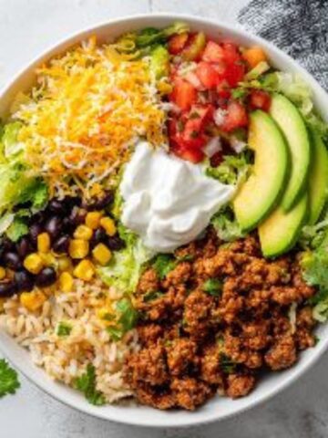 Taco rice bowl with cilantro lime rice, ground beef, beans, corn, and fresh toppings