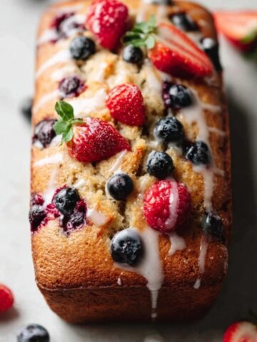 Moist very berry loaf cake with glaze on white kitchen counter