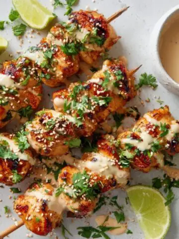 Juicy homemade bang bang chicken skewers drizzled with creamy sauce on a white kitchen counter