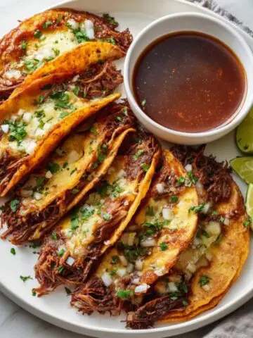 Authentic birria tacos with dipping consommé on white kitchen counter