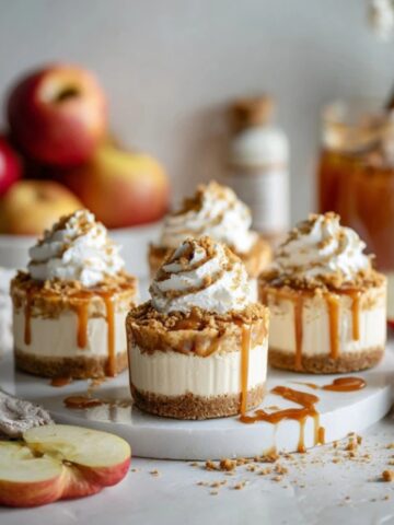 layered caramel apple dessert cups with caramel drizzle and whipped cream on white kitchen counter