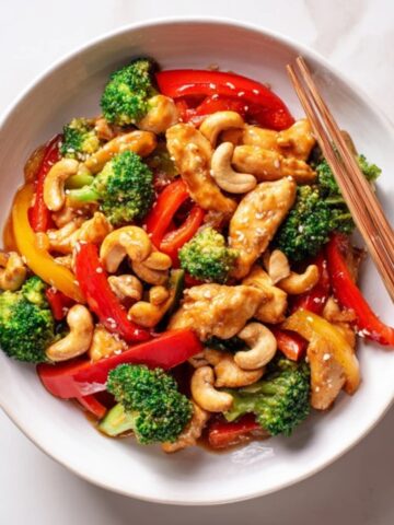 Homemade cashew chicken stir fry with colorful vegetables and cashews in a white bowl.