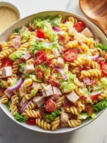 Creamy club sandwich pasta salad with bacon, turkey, ham, and cheddar in a white bowl.