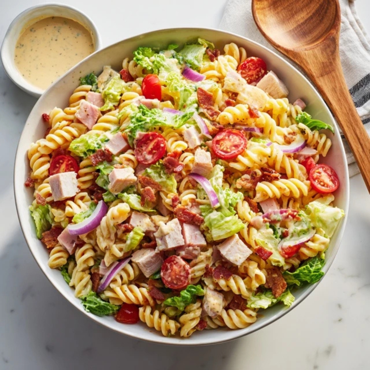 Creamy club sandwich pasta salad with bacon, turkey, ham, and cheddar in a white bowl.