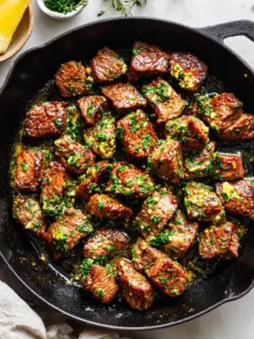 Garlic butter steak bites in a cast-iron skillet on white counter