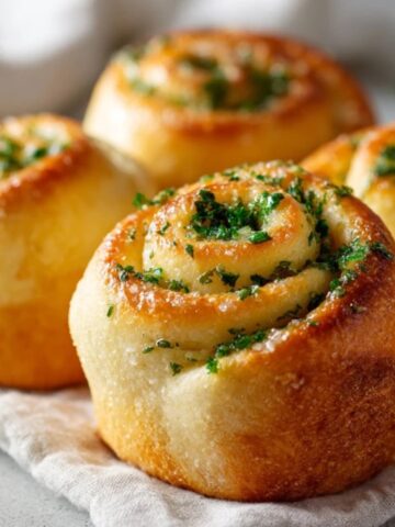 Soft homemade garlic swirl rolls brushed with melted butter and parsley on a white kitchen counter