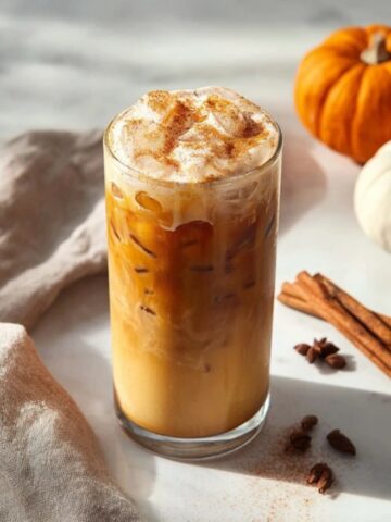 Homemade iced pumpkin cream chai tea latte topped with pumpkin cold foam on a white kitchen counter