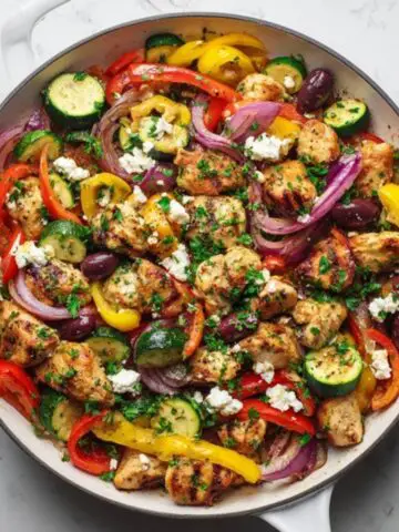Mediterranean chicken stir fry with colorful vegetables and feta cheese in a white skillet.
