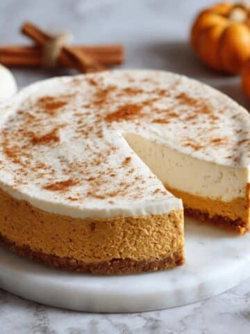 Homemade pumpkin cheesecake on white counter with creamy topping
