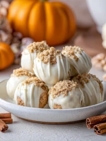 No-bake pumpkin cheesecake balls coated in white chocolate on a kitchen counter