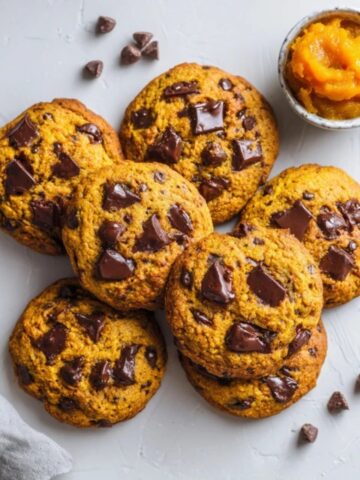 Soft and chewy homemade pumpkin chocolate chip cookies with melted chocolate chips on a white counter, perfect fall dessert recipe.