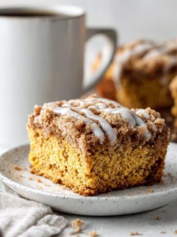 Moist pumpkin coffee cake with cinnamon streusel topping and vanilla glaze on a white kitchen counter