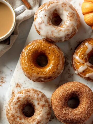 Homemade pumpkin donuts with maple glaze and cinnamon sugar on a white kitchen counter.