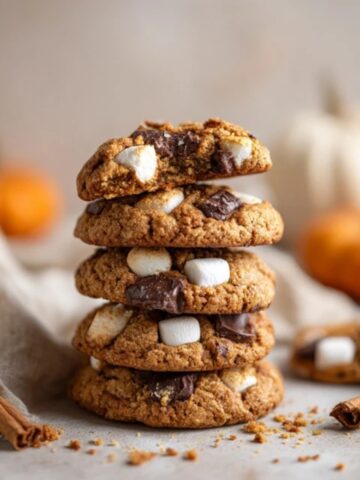 Homemade pumpkin s’mores cookies stacked on white kitchen counter with gooey marshmallows and chocolate.