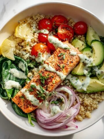 Healthy salmon quinoa bowl with veggies and lemon herb dressing on a white kitchen counter