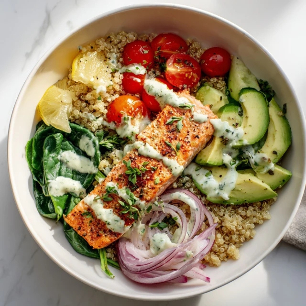 Healthy salmon quinoa bowl with veggies and lemon herb dressing on a white kitchen counter