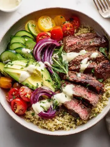 Healthy steak quinoa bowl with avocado and veggies on white counter