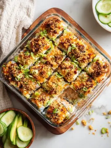 Homemade sushi bake in a glass dish topped with furikake, avocado, and cucumber — creamy, baked layers of rice, crab, and sriracha mayo.