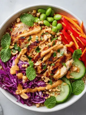 Colorful Thai quinoa bowl with peanut sauce and fresh vegetables on white kitchen counter