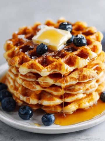Homemade gluten free waffles with butter and maple syrup on white kitchen counter