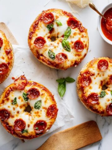 Homemade pizza bagels topped with melted mozzarella and basil on a white kitchen counter