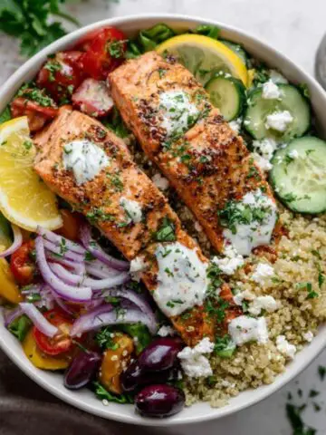 Mediterranean salmon bowl with quinoa, veggies, and feta on white counter